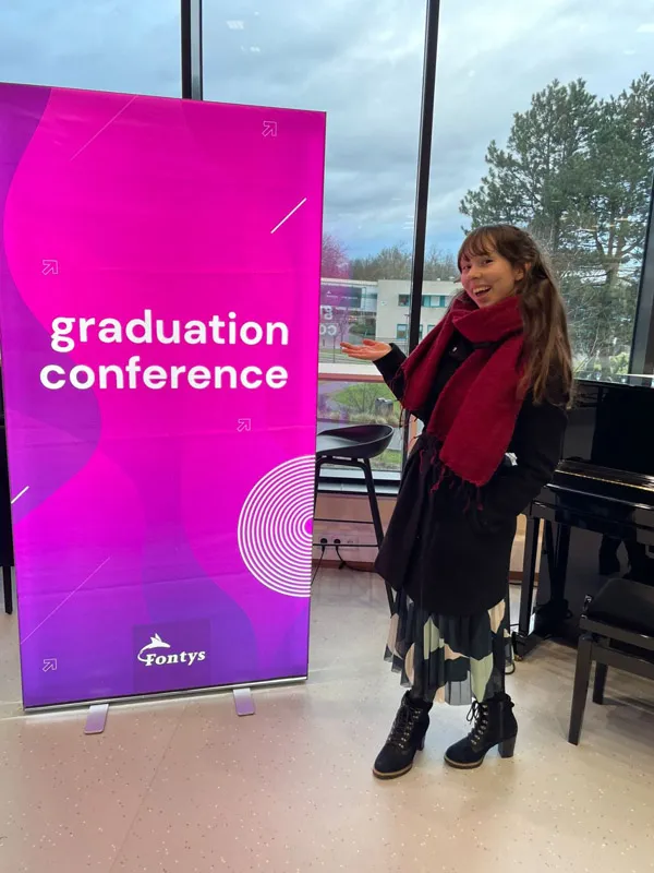Eline stands in front of a banner that reads ‘graduation conference, fontys’
