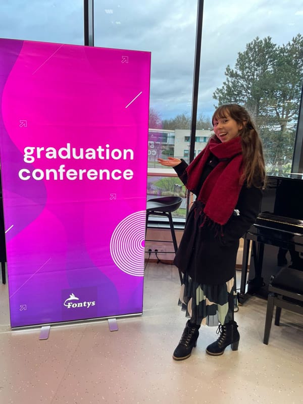 Eline staat voor een banner waar op staat: "graduation conference, fontys"